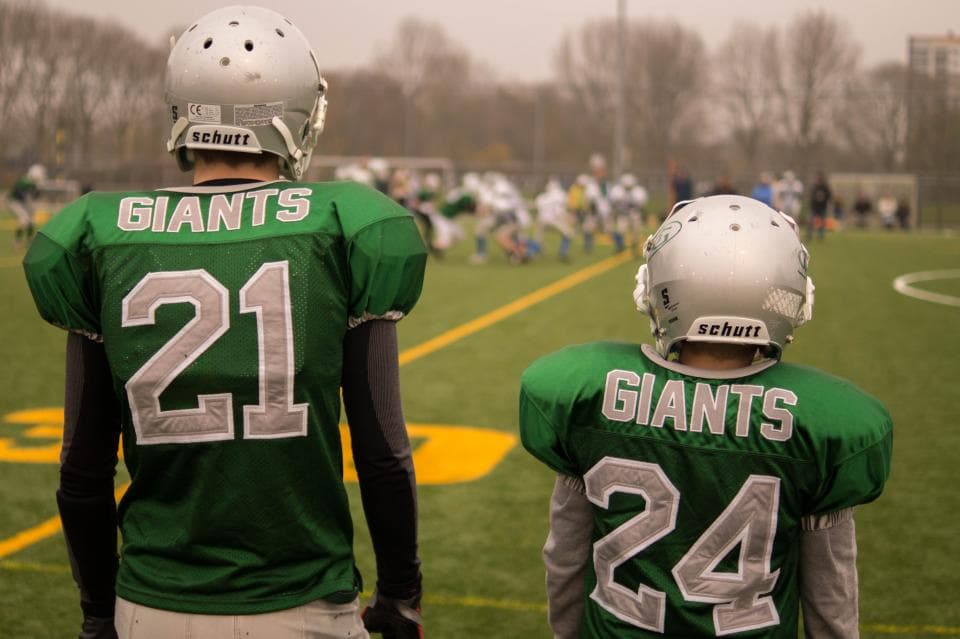 Deux jeunes joueurs en maillot de club, vus de dos au bord du terrain